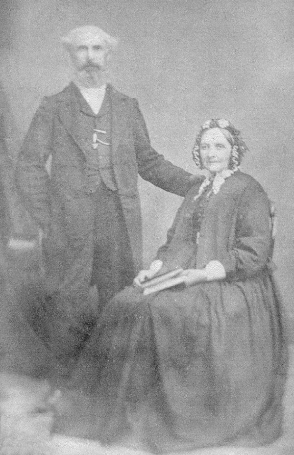 Photo of Thomas standing left and Ann sitting to his right